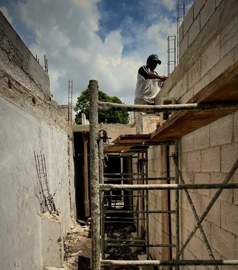 A mason working on scaffolding along a new block wall during construction